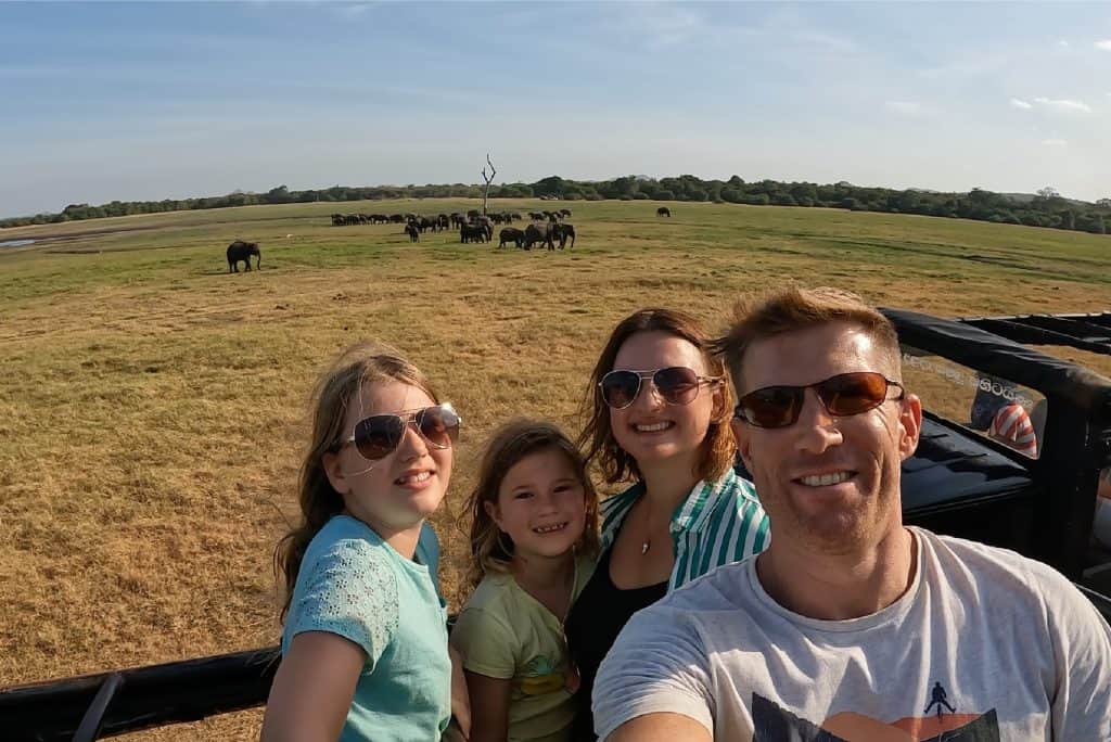 Tin Box family pose in jeep with herd of elephants in the background at Kaudulla National Park