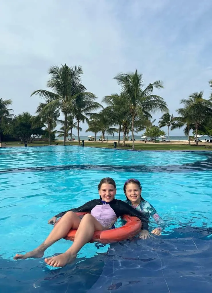 Girls playing in outdoor swimming pool at Calm Resort in Pasikudha with palm trees and beach in background