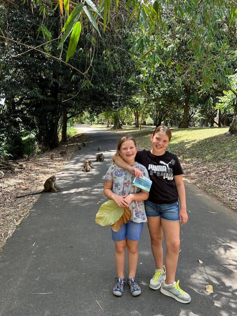 Our daughters stood on a path in the Royal Botanical Gardens with a family of monkeys behind them