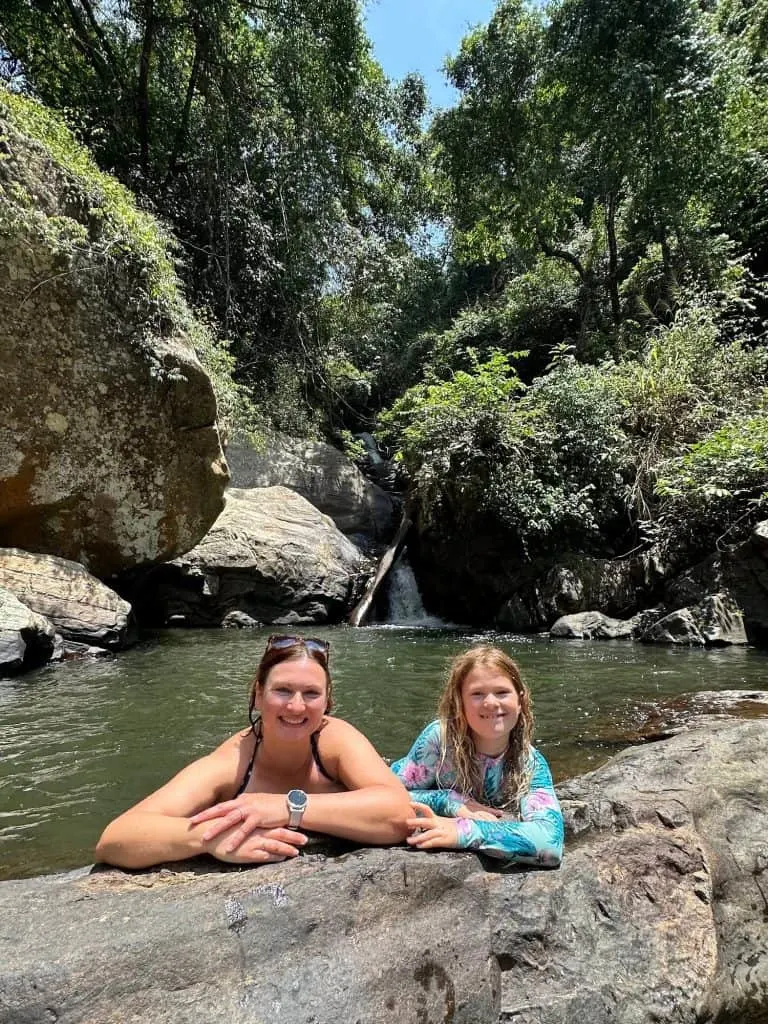 Claire and eight year old daughter on the edge of pool under a waterfall