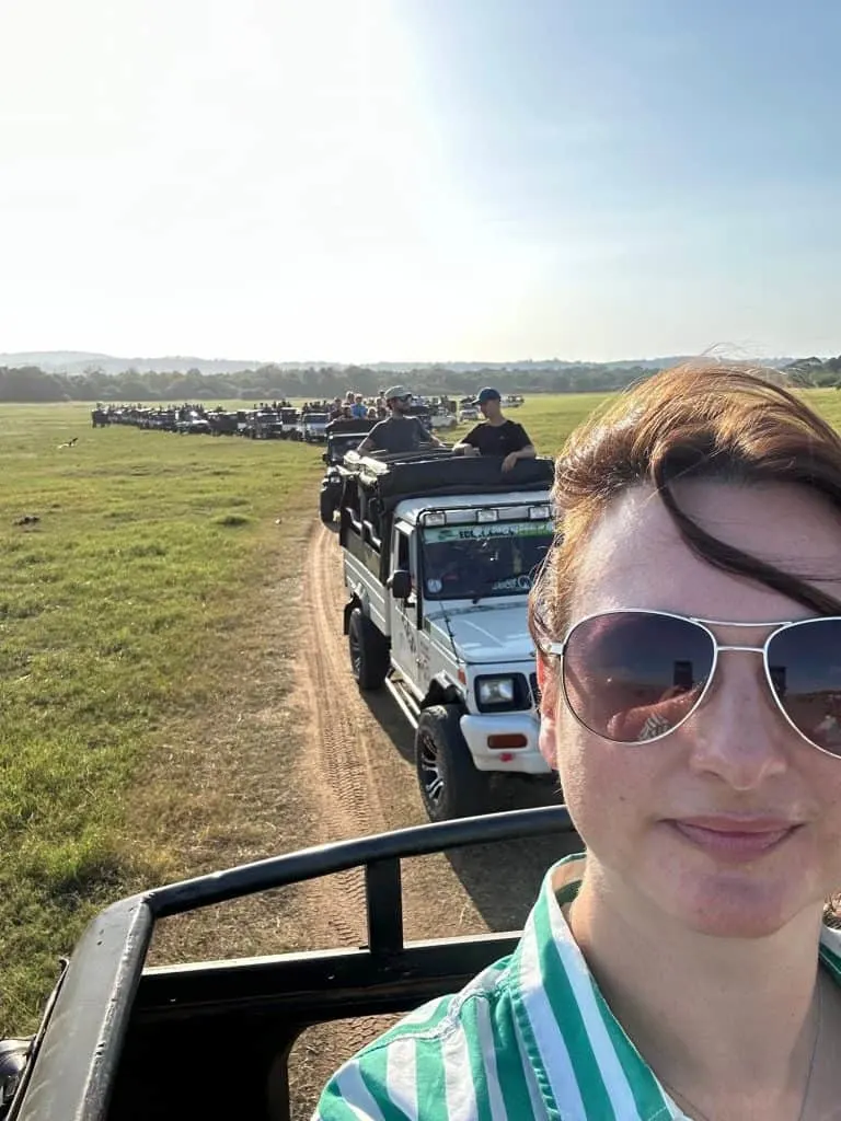 Claire looks at camera with a view of dozens of jeeps lined up on the road behind her