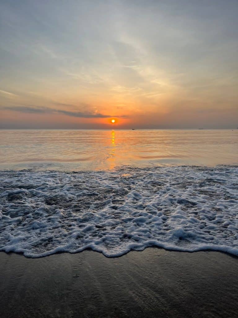 Waves ripple up the sand on Pasikudah beach with the sun rising on the horizon