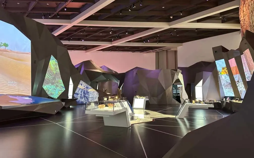 The Land of Oman exhibition area in Oman Across the Ages museum. The space includes high tech screens alongside prehistoric exhibits behind glass