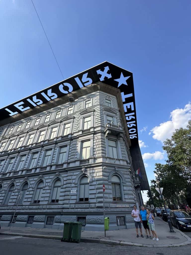The outside of the House of Terror Museum. It's an apartment style building from the 20th Century with an over hanging metal roof. Cut into is the words Terror on two sides of the building