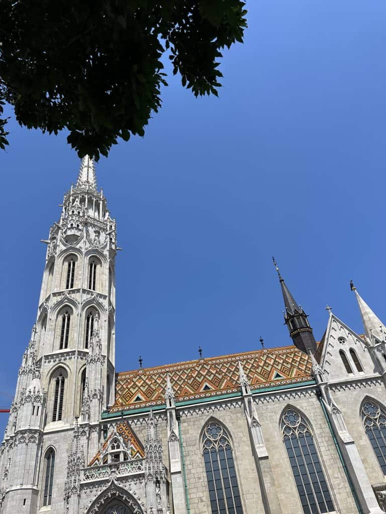 Looking up at Matthias Church which has an intricate tiled roof. The church is gothic in style
