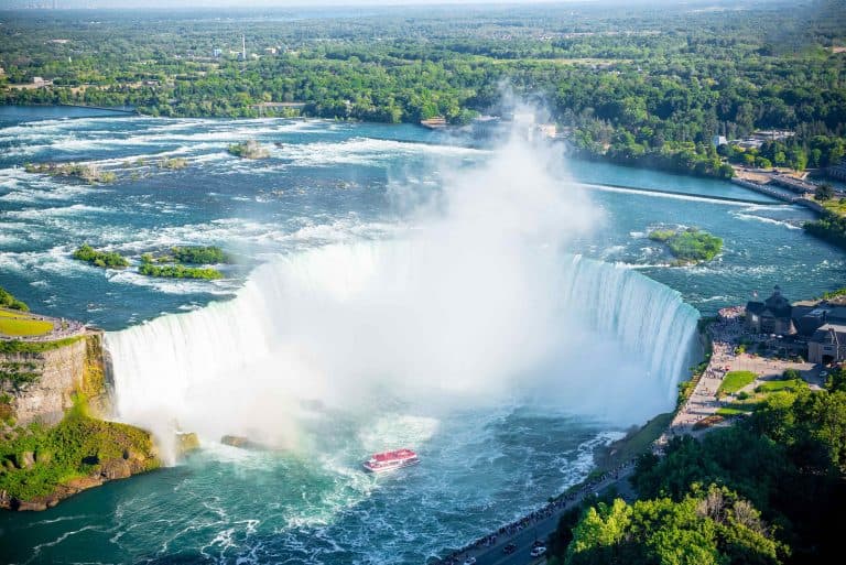Aerial view of Niagra Falls. A red tourist boat is below the falls and you can see the countryside beyond