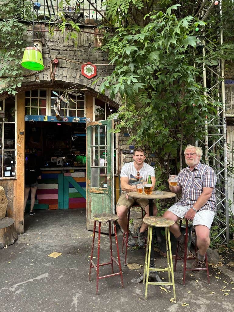 Mr Tin Box and his dad sat on stools at a high table in a ruin bar. There are beers on the table