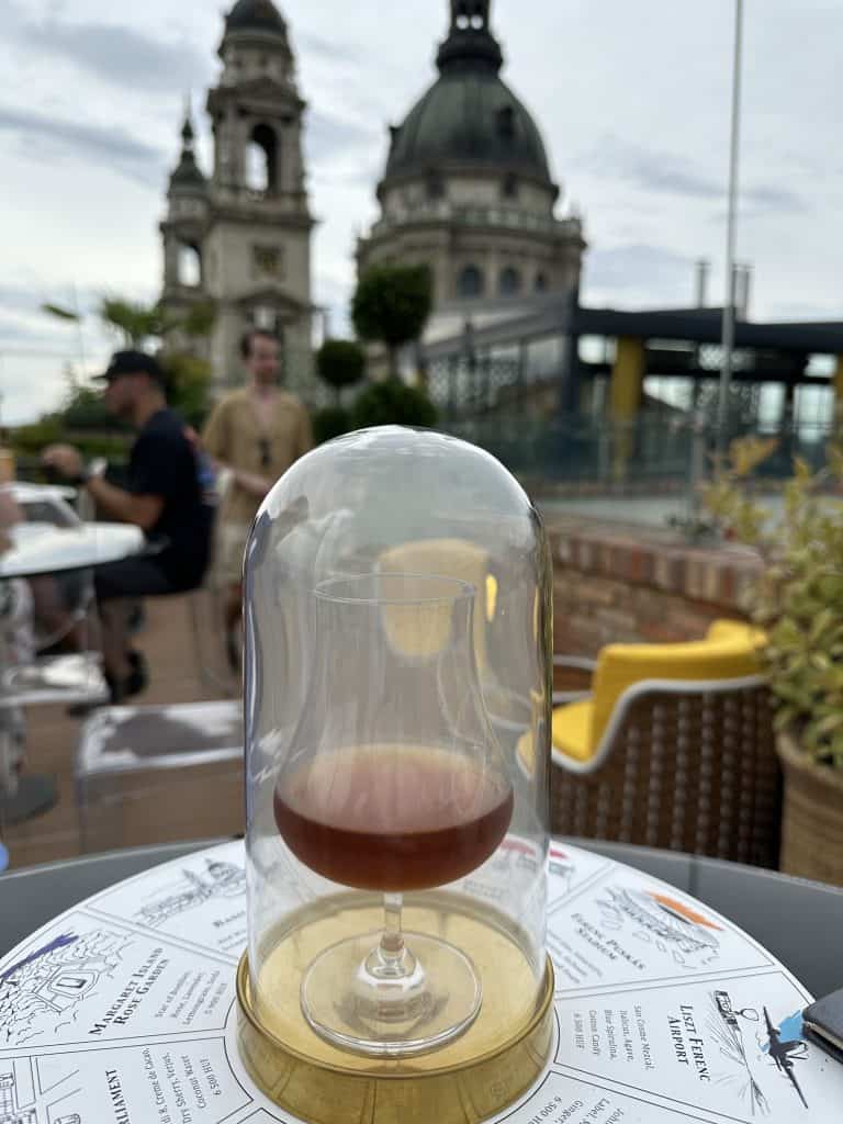 A glass of hot brown liquid inside a glass dome. There's smoke inside the dome.