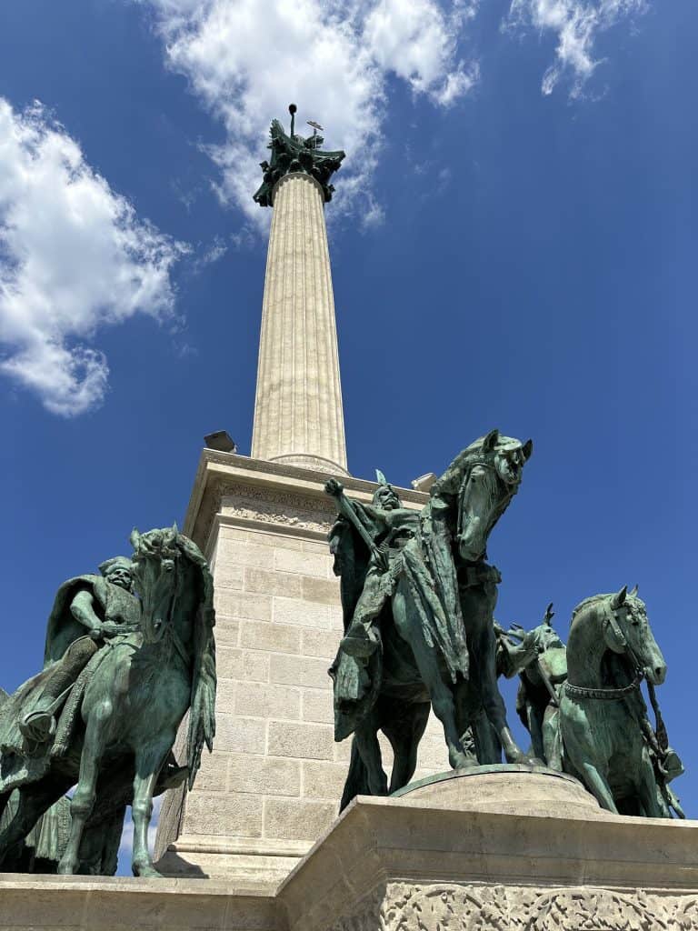 Statues of Hungarian tribal leaders on horseback below a tall white stone column in Heroes Square in Budapest
