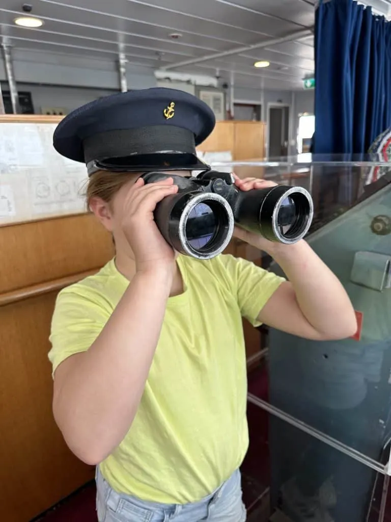 Our eight-year-old looking out of the bridge window with a pair of binoculars. She is wearing a captain's hat