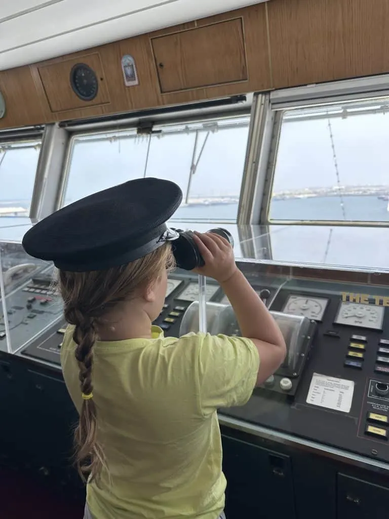 Our eight-year-old looking out of the bridge window with a pair of binoculars. She is wearing a captain's hat