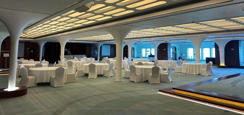 Dining tables and covered chairs in the Queen's Room lounge on the QE2