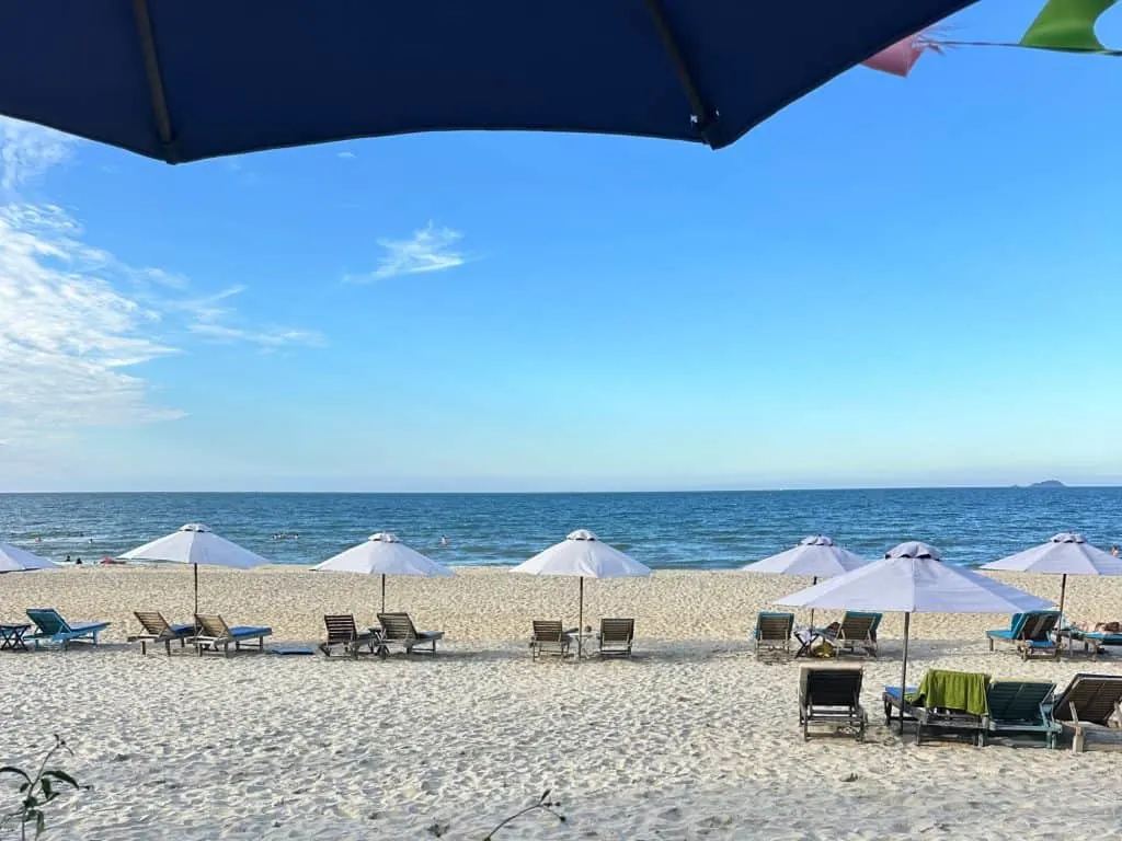 A view of the sand and a row of sun loungers at An Bang beach. The sea and sky beyond are blue.