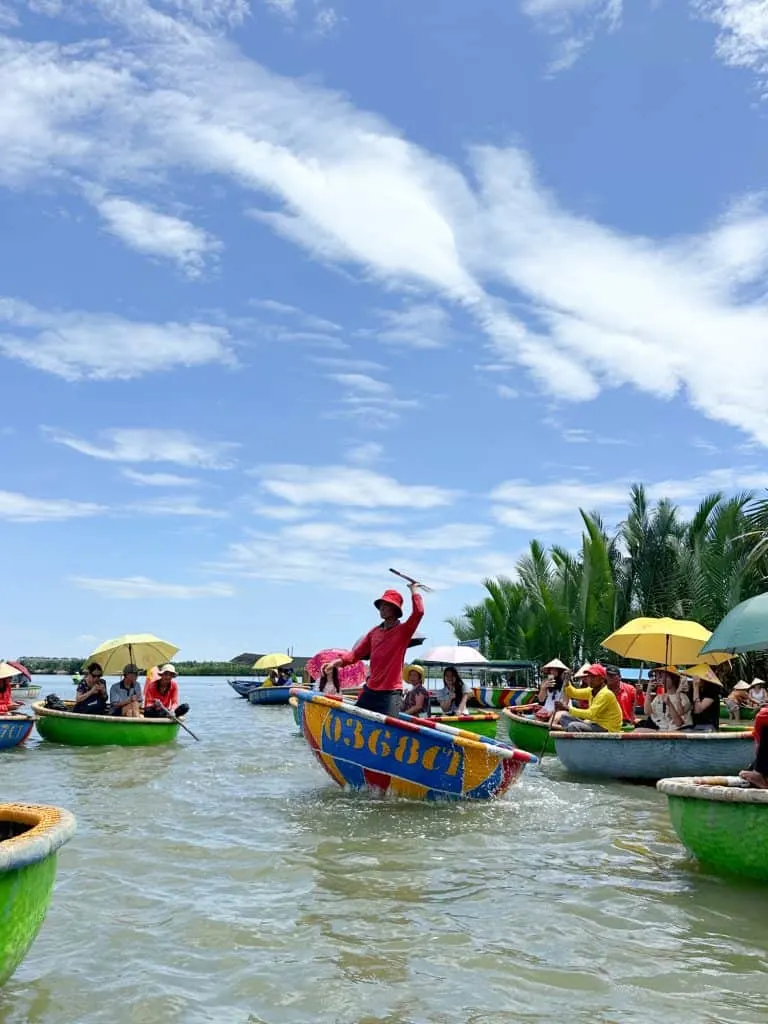 A man stands in a spinning bucket boat while lots of tourists watch him perform