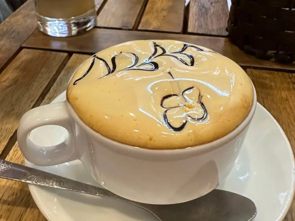 A tea cup of frothy coffee with a floral design on top