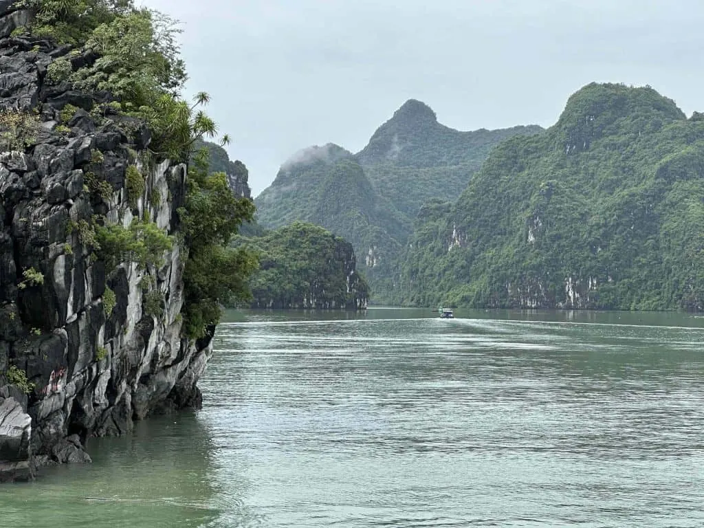 A close up of the limestone mountains of Ha Long Bay looking towards a boat sailing into a cove