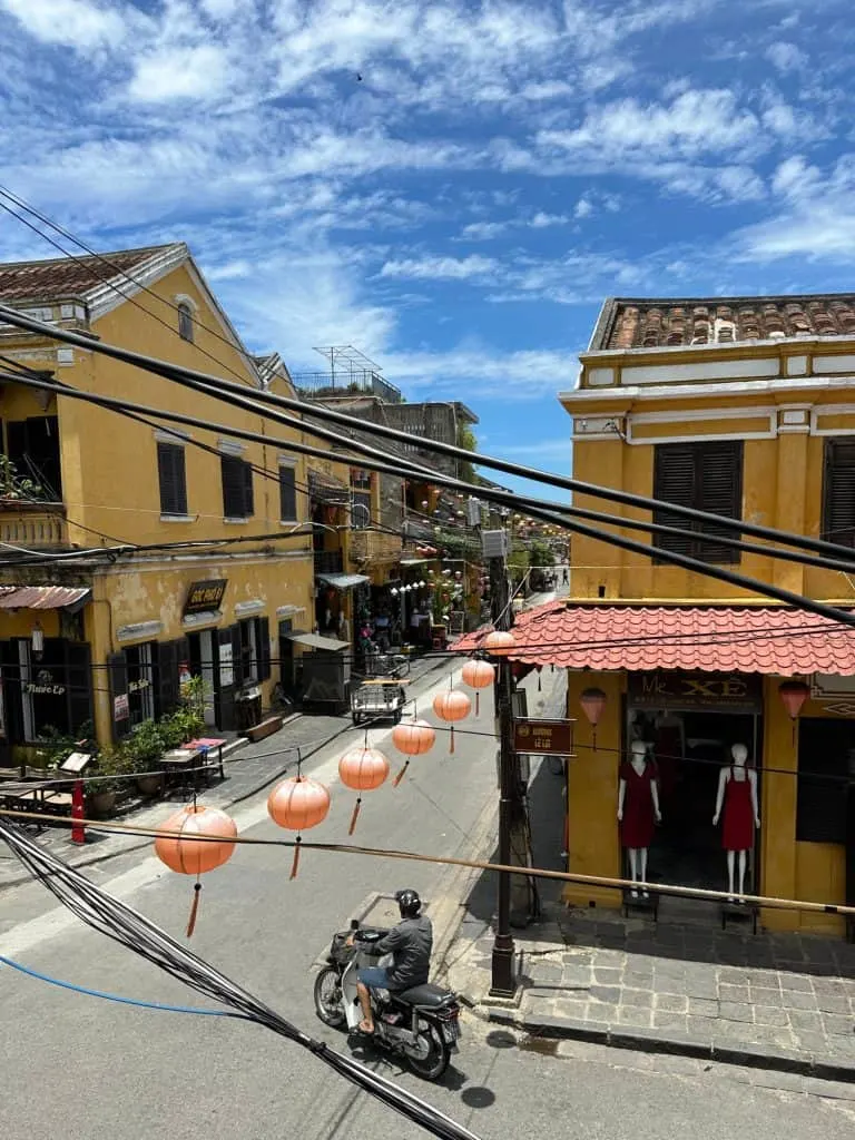 A view of a Hoi An Street from above. There are power cables in front of the view. The low level buildings are painted yellow.