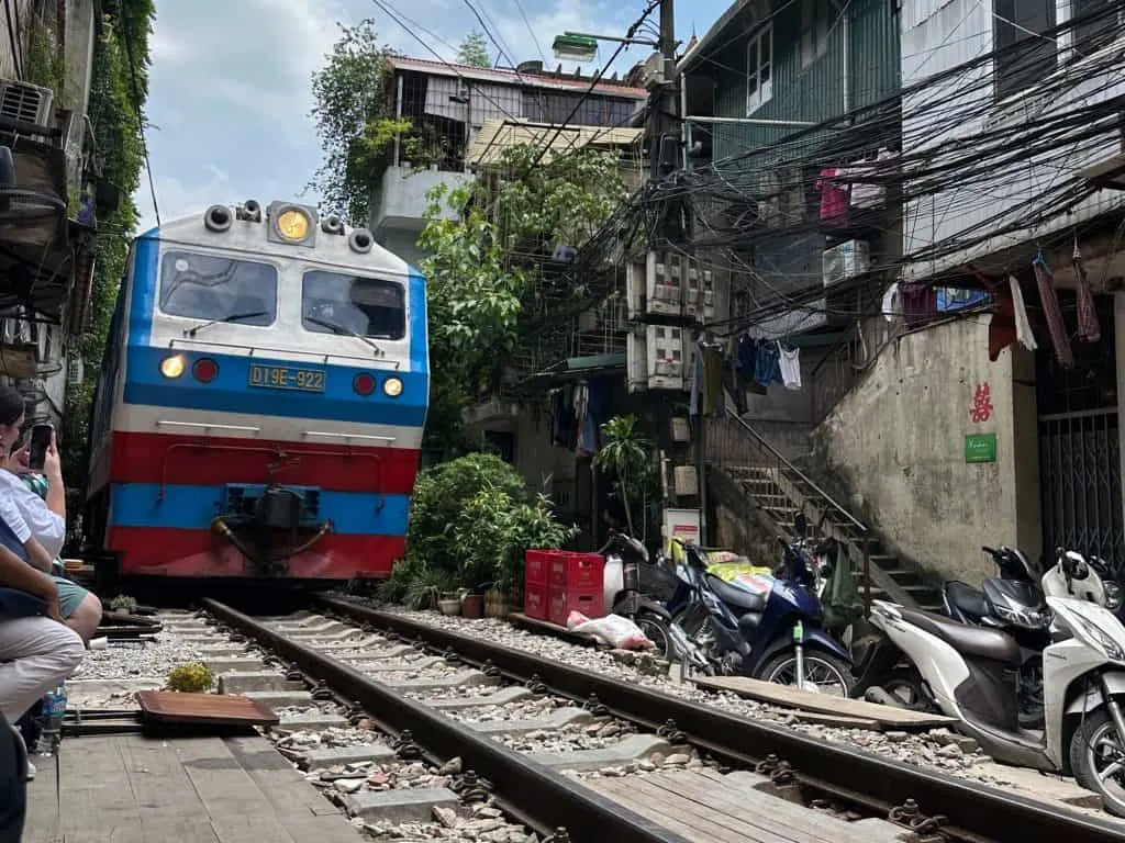 A blue and red train coming down the tracks of Train Street in Hanoi