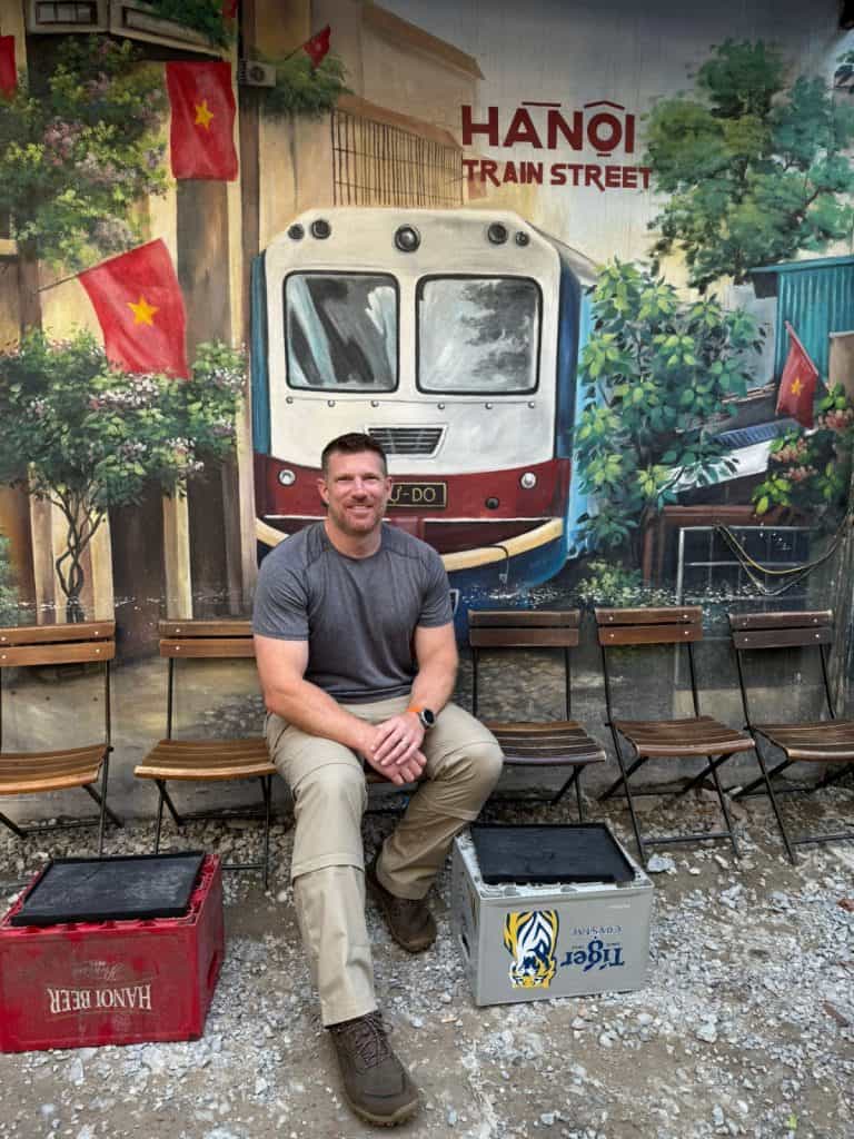 Mr Tin Box sat in front of a mural of a train on Train Street in Hanoi