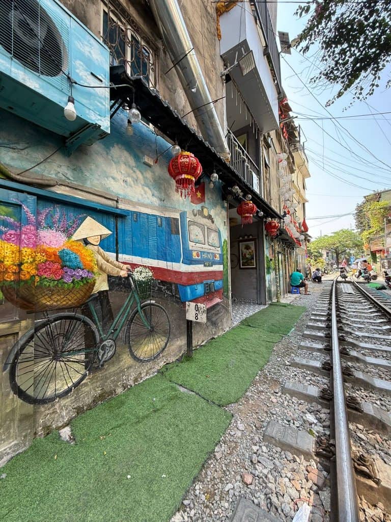 A mural of a traditionally dressed Vietnamese women with a bike in front of a train painted on a wall on Train Street in Hanoi