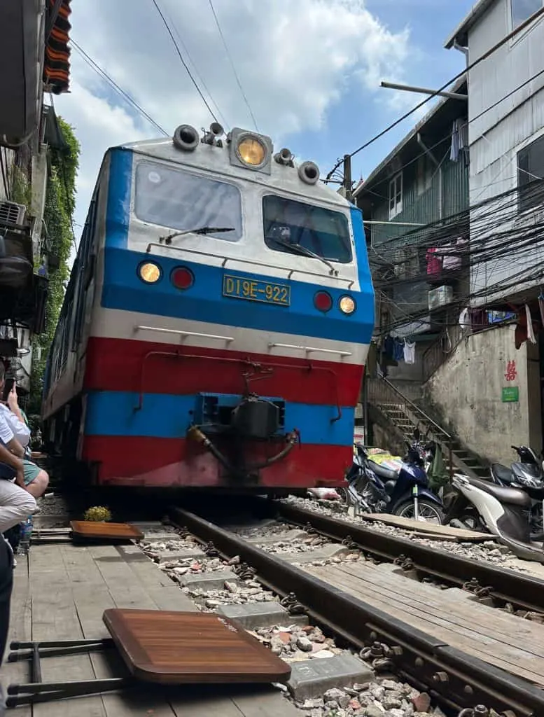 A blue and red train coming down the tracks of Train Street in Hanoi