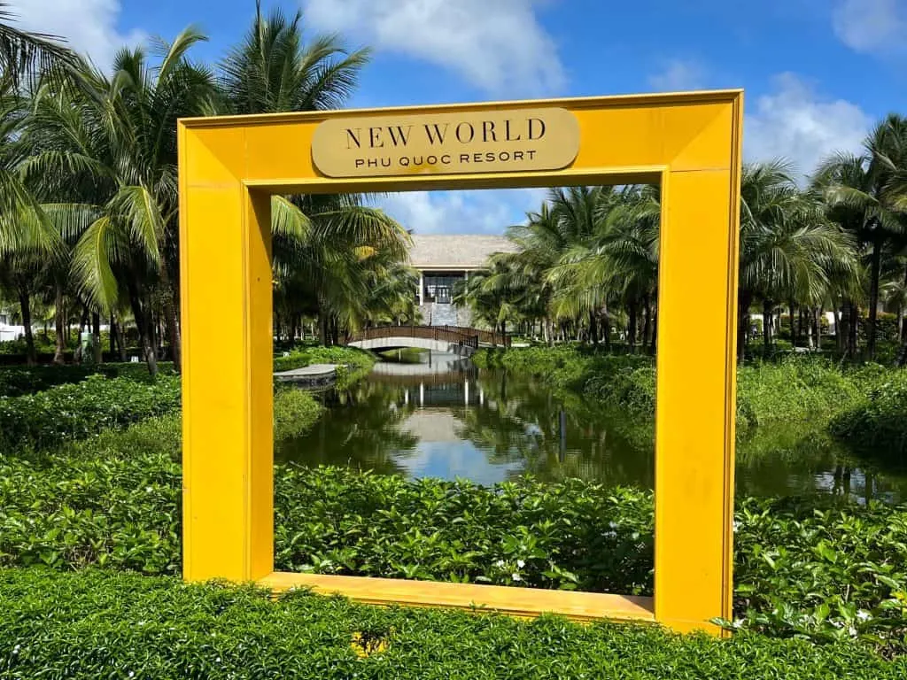 A yellow picture frame through which you can see palm trees and the New World Phu Quoc Resort reception. building in the distance