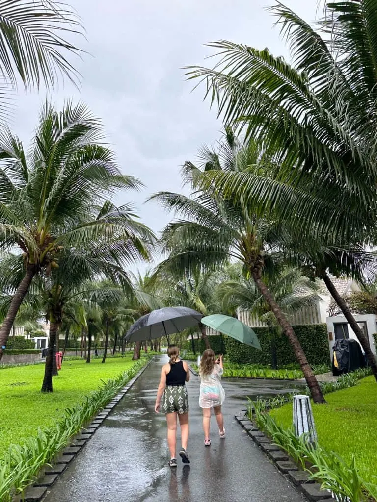 Our daughters walking away through a palm lined street with umbrellas over their heads