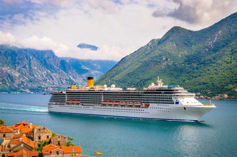 A cruise ship sailing along the coast of Montenegro. Terracotta tiled houses are in the foreground ands mountains behind