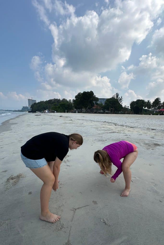 My daughters bent over looking at tiny camouflaged crabs on the beach in Langkawi