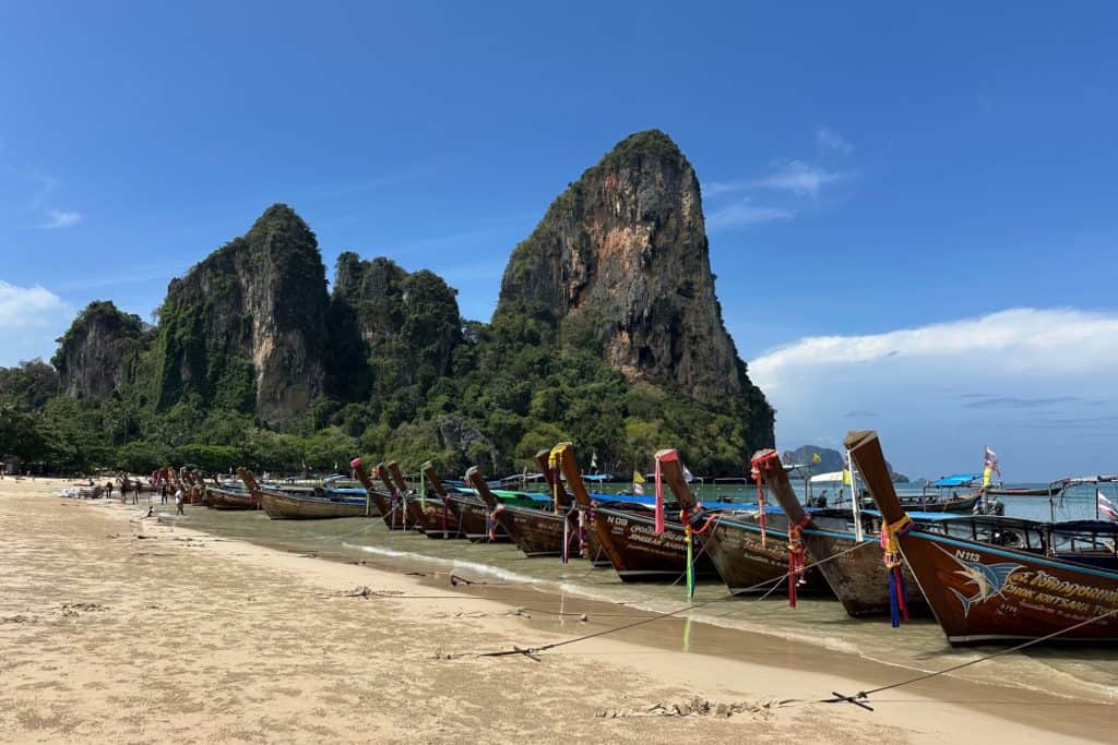 Longtail speed boats lined up along the beach at Railey in Krabi. The jungle covered limestone cliffs are in the background