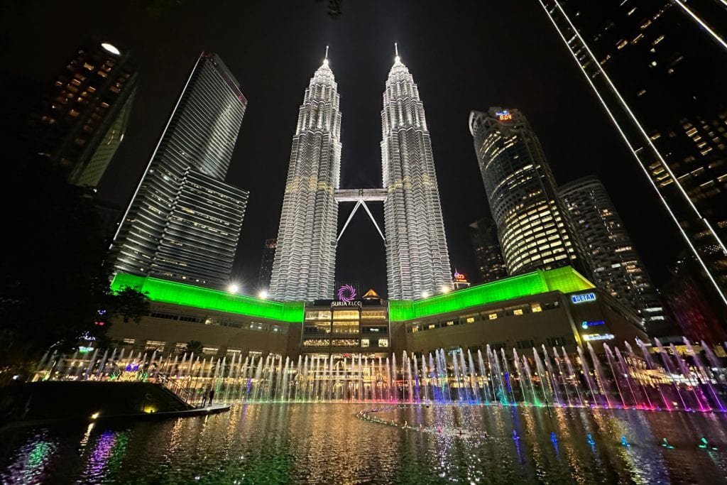 A view from the Petronus Towers fountains looking up towards the towers which are illuminated against a night sky