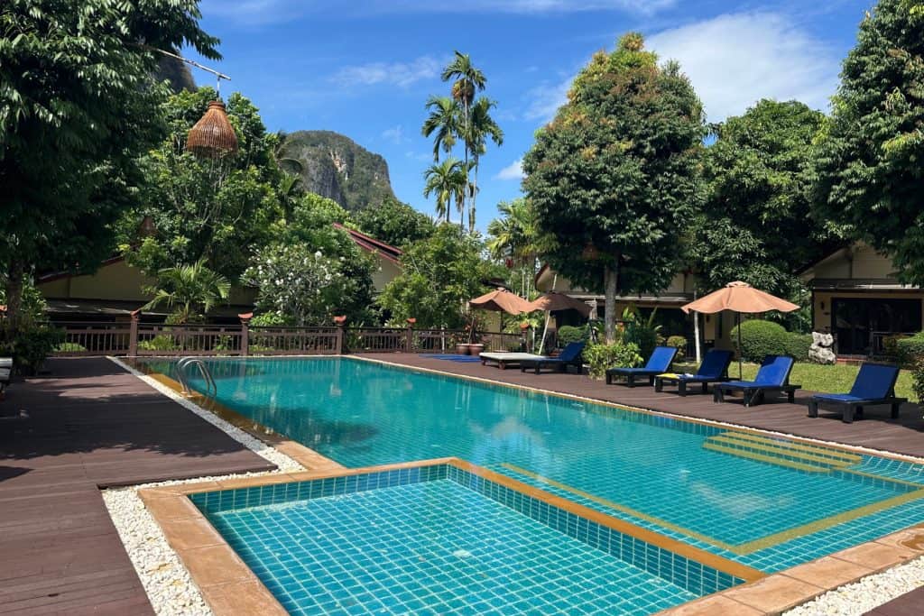 The outdoor swimming pool at Aonang Phu Petra in Krabi. There are palm trees and limestone cliffs in the background