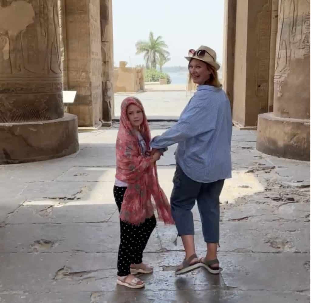 Me and my daughter walking through a temple in Egypt and looking back at the camera. I am wearing cropped trousers and a long sleeved shirt