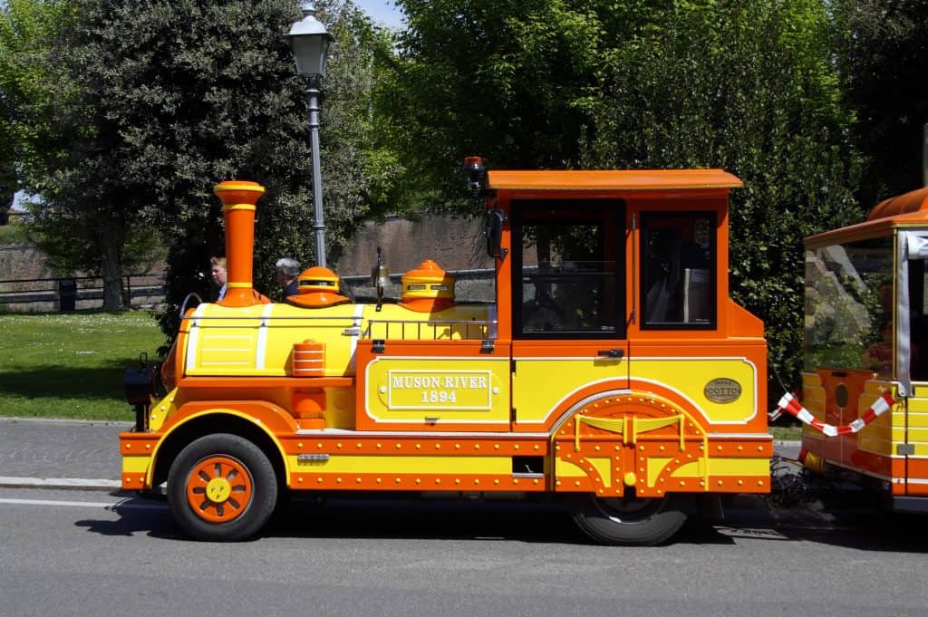 Peschiera, Italy - April 21, 2019: Orange and yellow colored trackless tourist locomotive train or Dotto train by the side of the road.