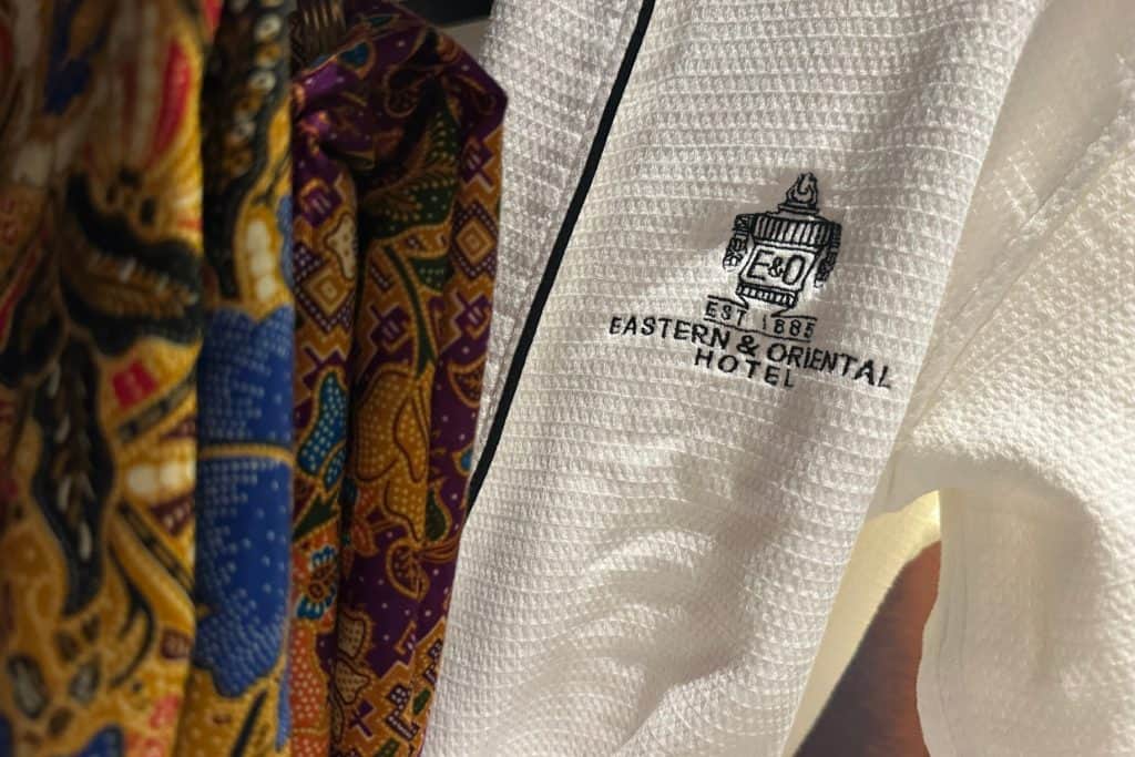 A white E&O bath robe hanging next to brightly patterned sarongs in the walk in wardrobe of our suite at the E&O hotel