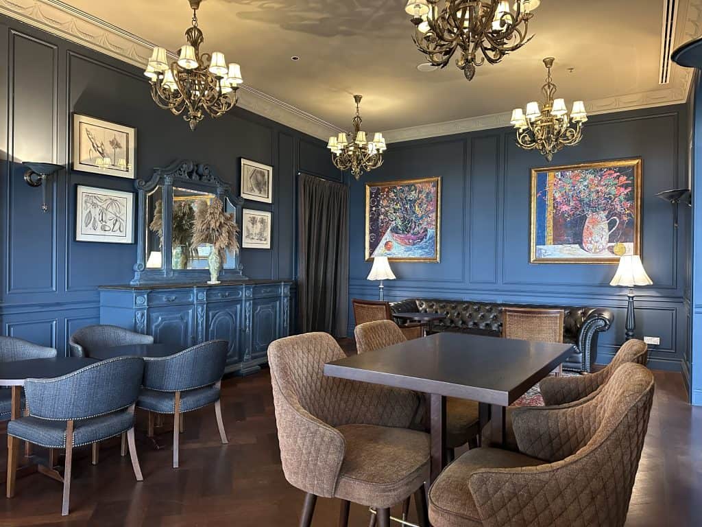 Seating in Farquhar's Bar at the E&O. The area is richly decorated with dark blue walls, chandeliers and leather bar seats