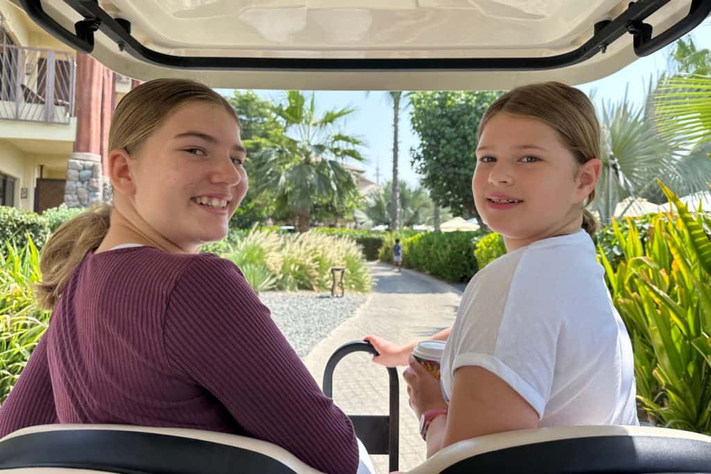 Mis hijas mirando hacia atrás por encima del hombro mientras viajan en uno de los carritos de golf del resort Lapita Hotel.