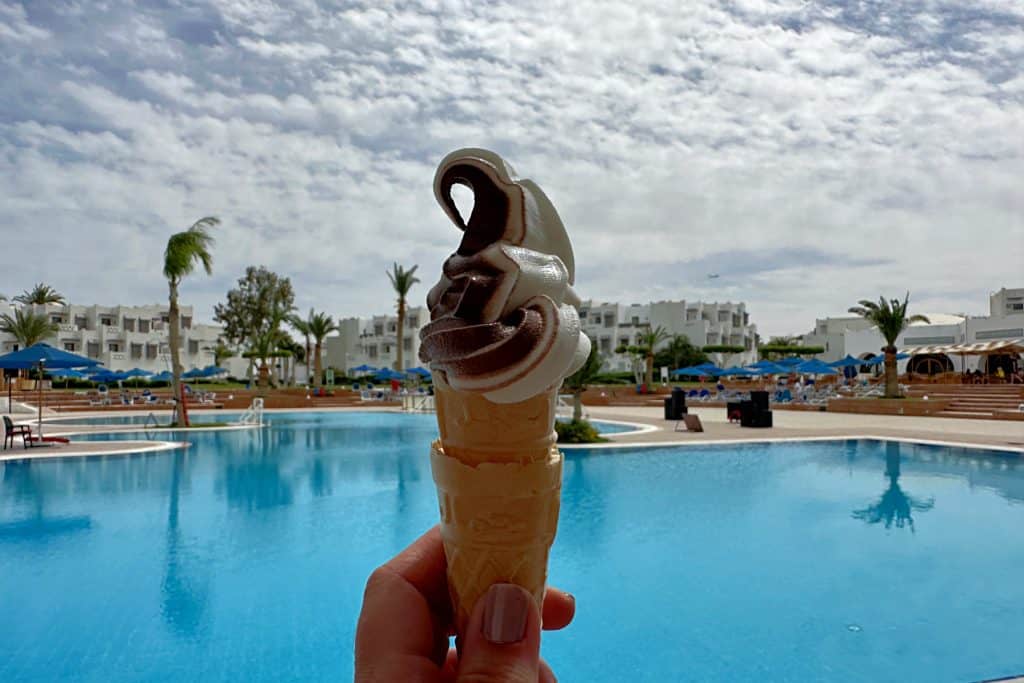 Mi mano sosteniendo un cono de helado batido de chocolate y vainilla en el complejo de piscinas del Mercure Hurghada
