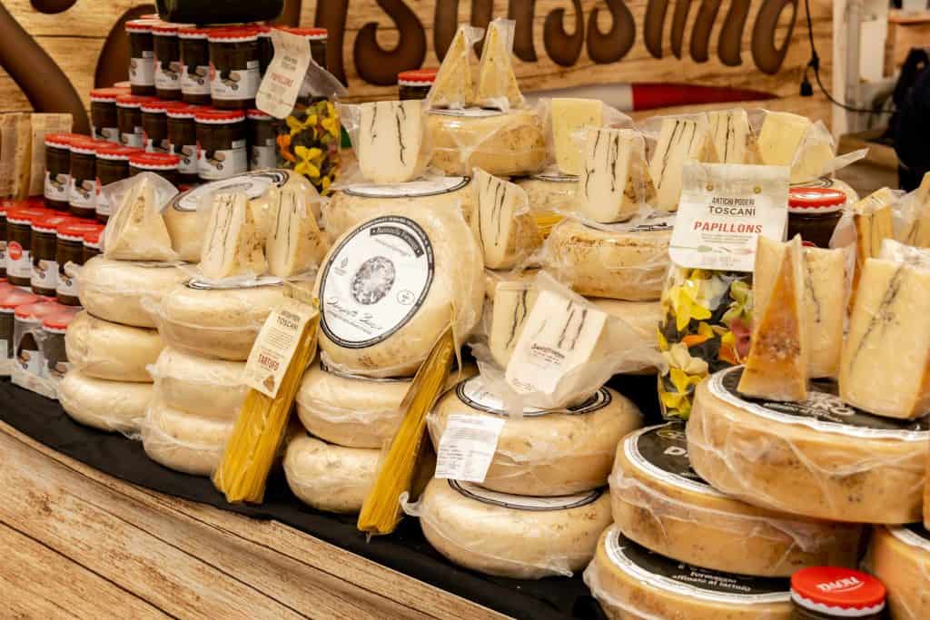 Assorted vacuum packed artisan cheese wheels, wedges and pasta on a rustic market stall counter, gourmet delicatessen display with truffle varieties, jars and Italian specialty foods