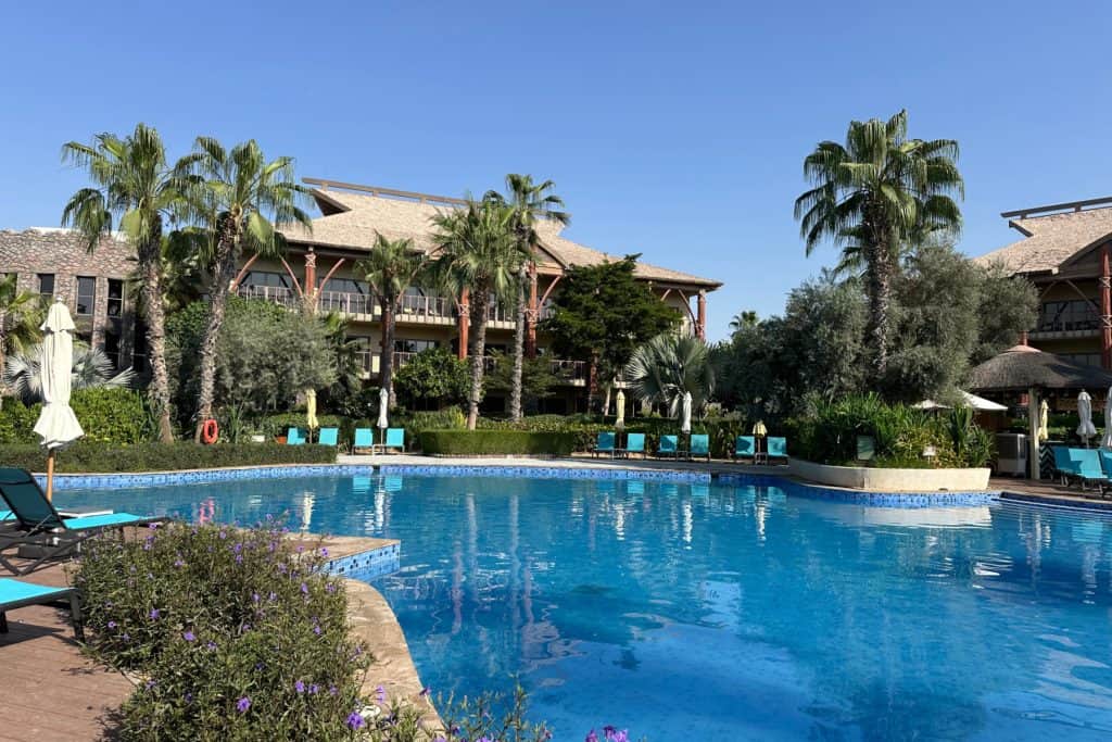 La zona de la piscina del Lapita Hotel Dubai por la mañana. Está tranquilo. Alrededor de la piscina hay árboles y detrás de ellos está uno de los bloques del hotel con vistas al agua.
