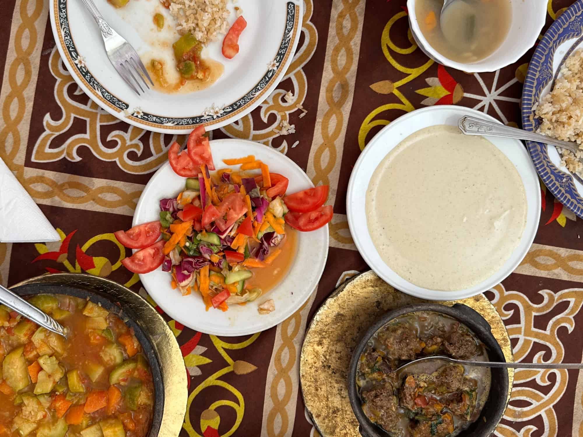 Platos tradicionales egipcios sobre un mantel de colores brillantes. La comida incluye ensalada, taggine de hummus y sopa Orzo.