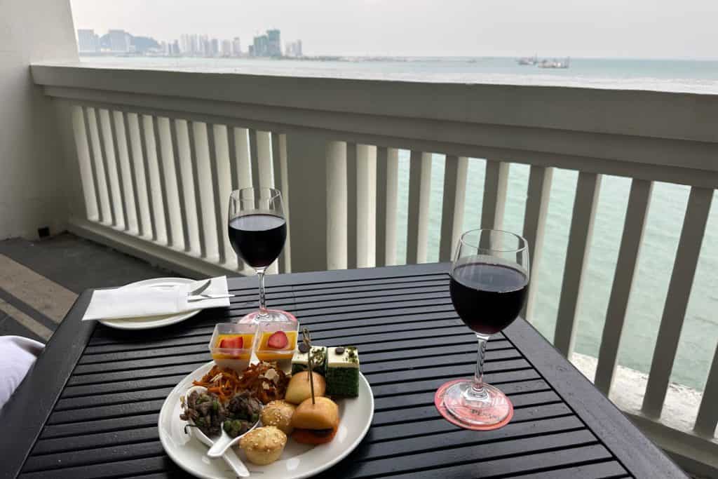 A substantial plate of canapes and two glasses of red wine on a balcont table overlooking the sea and Penang