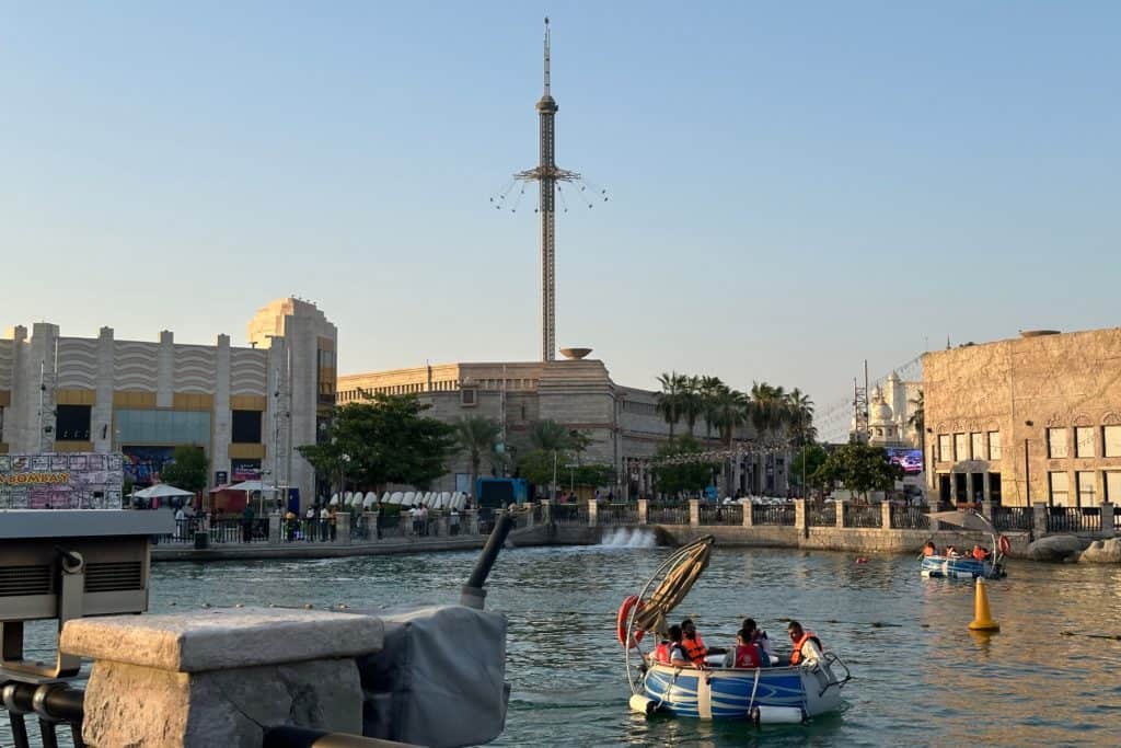 Una vista de uno de los lagos de Riverland Dubai. La gente flota en botes en el agua y al fondo se puede ver una atracción alta en el Real Madrid World.