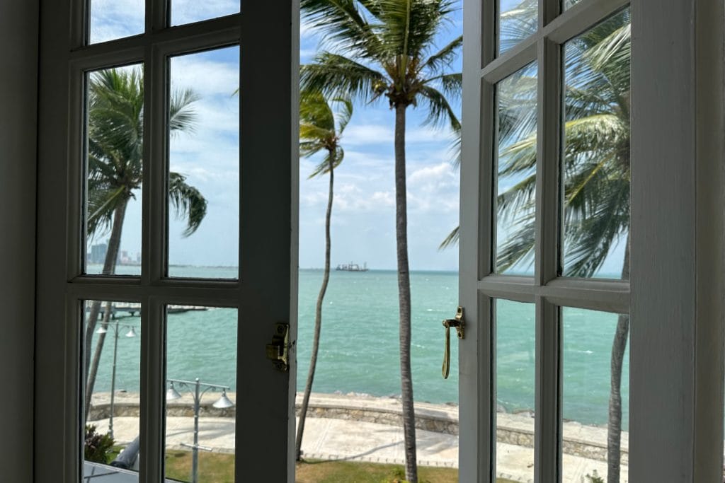 The view from our heritage wing suite window onto the turquoise sea through palm trees