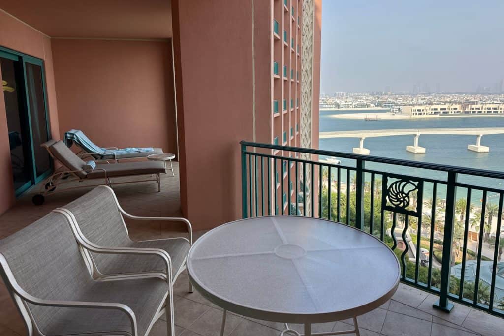 A view across a table a chairs towards two sun loungers on our Terrace Suite balcony with Jumeirah Palm and Dubai in the background