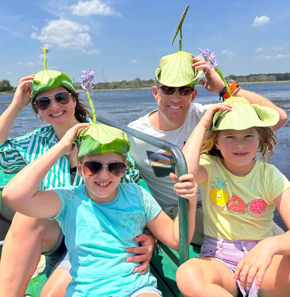 The Tin Box family sat in a double kayak wearing water lily hats. They are on holiday in Sri Lanka