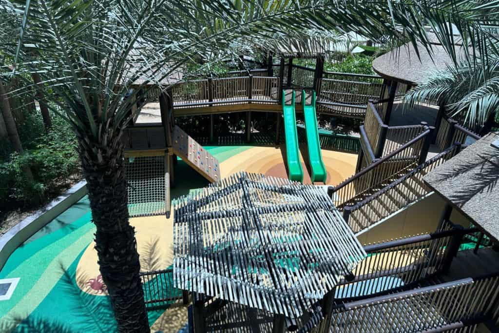 A view of the Explorers Club outdoor play area from above. There is a play fort with slides shaded by palm trees