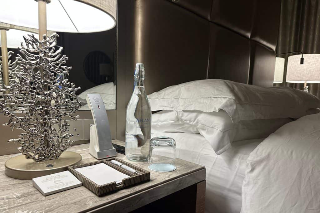The bedside table in the master bedroom with. turned down bed and bottle of water on the side
