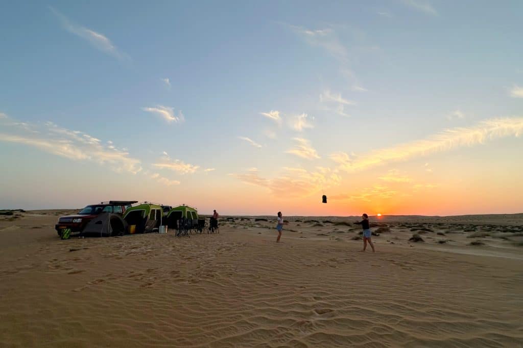Camping on the southern edge of the Wahiba Sands desert in Oman. The sun is setting over the dunes and the girls are playing catch