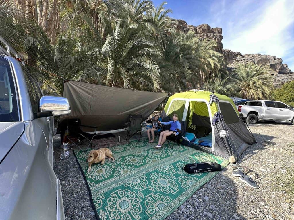 Our daughters and Tin Box dog in the shade between our Coleman tent and our car at the camping spot at Wadi Damm in Oman